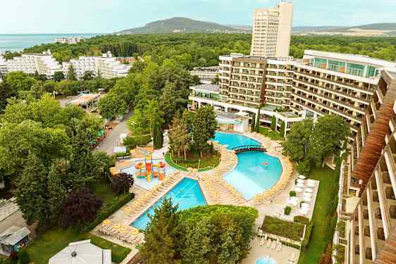 Utsikt över ett hotellområde med pooler, solstolar och omgivande träd. (AI-genererad text)