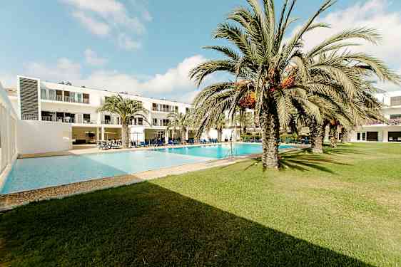 Hotellbyggnad vid en utomhuspool omgiven av palmträd och gräsmatta. (AI-genererad text)