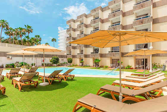 Utomhusområde med solstolar, parasoller och pool framför ett hotell. (AI-genererad text)