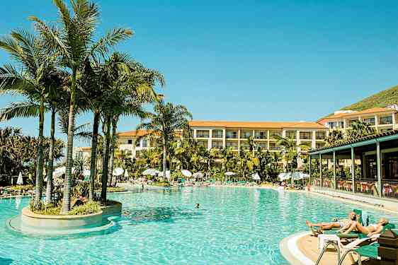 Uppvärmd utomhuspool omgiven av palmträd vid hotell med flera våningar. (AI-genererad text)