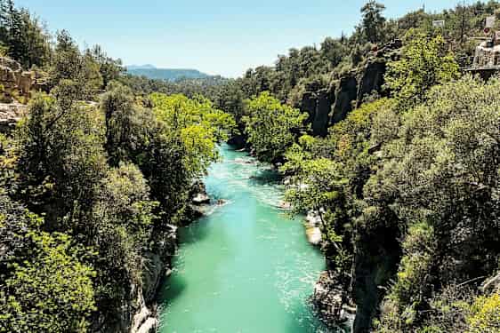 En turkosblå flod som flyter genom en grönskande ravin med klippor och träd. (AI-genererad text)