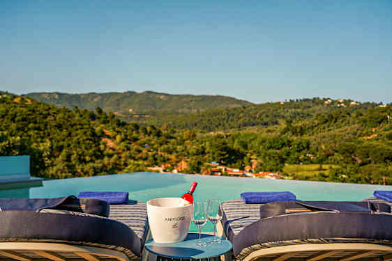 Solstolar vid en infinitypool med panoramautsikt över gröna berg och kullar. (AI-genererad text)