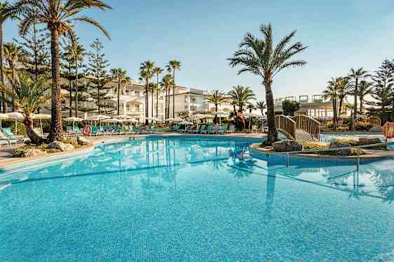 En utomhuspool omgiven av solstolar, parasoller och palmer vid ett hotell. (AI-genererad text)