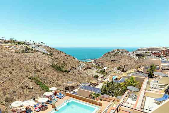 Vy över en pool, hotellbyggnader och landskap mot havet. (AI-genererad text)