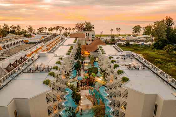 Flygbild av hotellkomplex med poolområde och solnedgång i bakgrunden. (AI-genererad text)