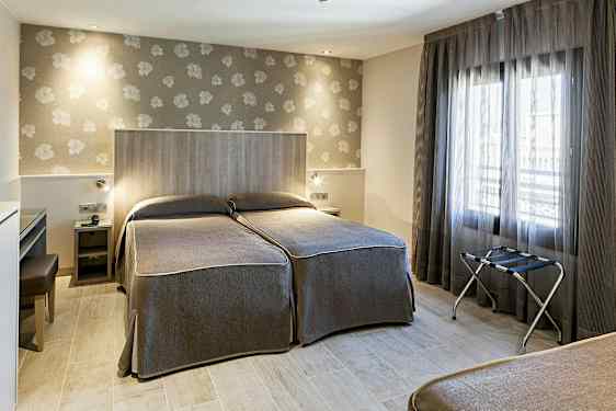 Ett hotellrum med två enkelsängar, tapetserade väggar och ett stort fönster med genomskinliga gardiner. (AI-genererad text)