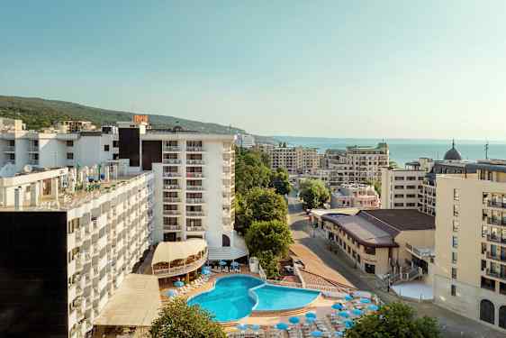 Hotellbyggnader med en utomhuspool och solstolar, omgivna av andra byggnader nära havet. (AI-genererad text)