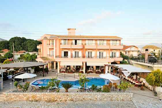 Ett hotell med peachfärgade fasader och en utomhuspool med omgivande sittplatser. (AI-genererad text)