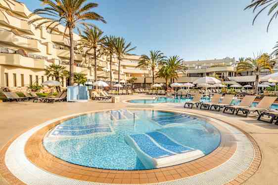 Ett poolområde på ett hotell med solstolar och parasoller runt poolen, omgiven av palmer och balkonger. (AI-genererad text)