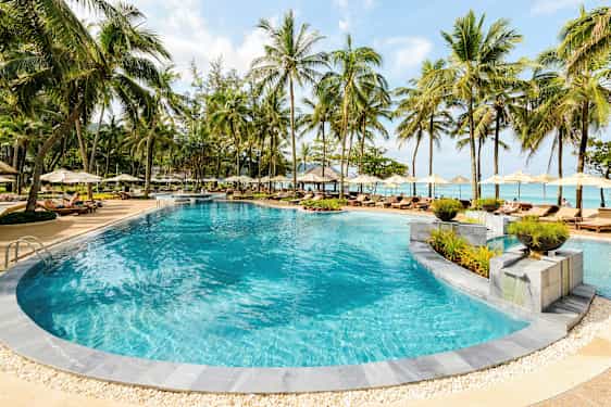 En utomhuspool omgiven av solstolar och parasoller vid en tropisk resort. (AI-genererad text)