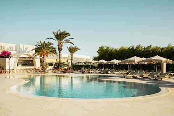 En utomhuspool med solstolar och parasoller, omgiven av palmer och en byggnad med en bar. (AI-genererad text)