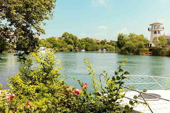 En flod med gröna buskar och träd vid dess kanter. En kejllik byggnad syns på höger sida. (AI-genererad text)