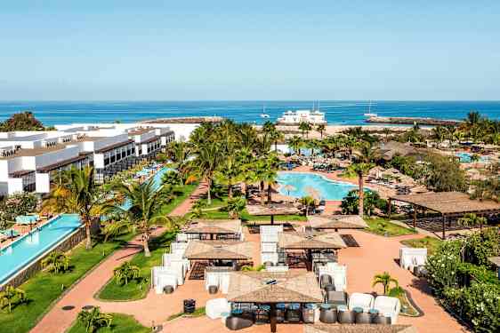 Semesteranläggning med vita byggnader, en swimmingpool och omgivande grönområde, samt hav i bakgrunden. (AI-genererad text)