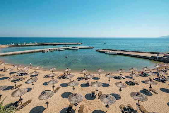 En strand med parasoller och solstolar vid en liten, lugn vik med klart vatten. (AI-genererad text)