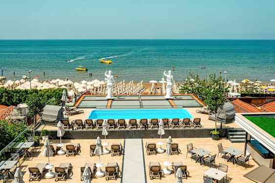 Utsikt över en pool med solstolar, statyer och en sandstrand vid havet. (AI-genererad text)