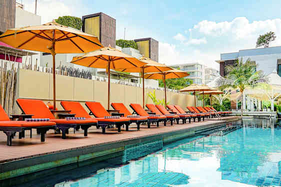 En utomhusbassäng med orangea solstolar och parasoller vid kanten, omgiven av modern arkitektur. (AI-genererad text)