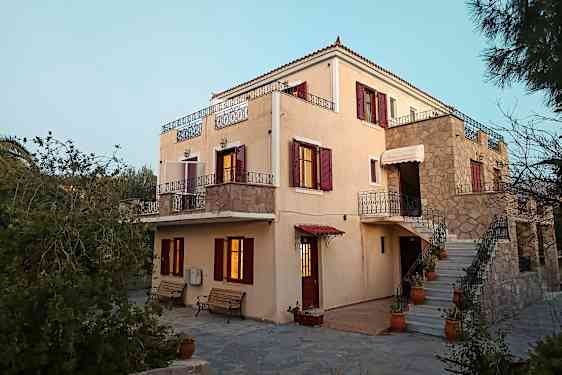 Ett ljus färgat hus med röda fönsterluckor och balkonger, omgiven av grönska. (AI-genererad text)