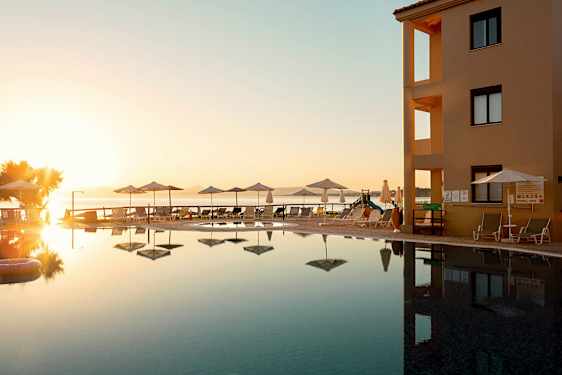 Ett poolområde vid en byggnad med utsikt över havet under en solnedgång. (AI-genererad text)