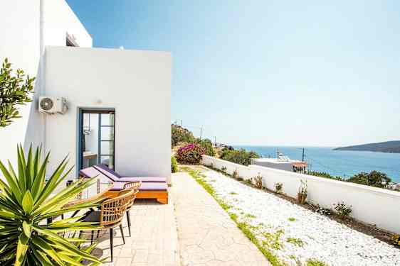 Vit byggnad med solstolar och bord på en uteplats mot en havsutsikt. (AI-genererad text)