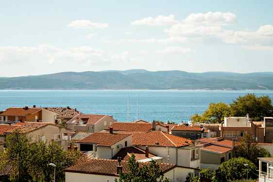 Röda tak på hus med havet och kullar i bakgrunden. (AI-genererad text)