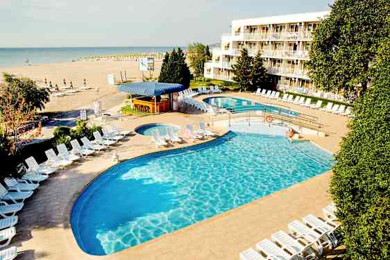 En hotellpool med solstolar och en strand i bakgrunden. (AI-genererad text)