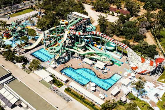 Ett vattenland med flera stora vattenrutschbanor, pooler och solstolar, omgiven av gröna träd och byggnader. (AI-genererad text)