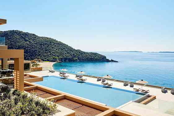 Utsikt över en pool med solstolar och parasoller, en kustlinje och hav i bakgrunden. (AI-genererad text)