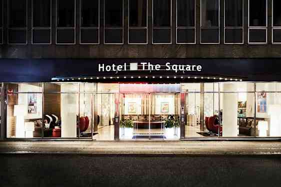 Fasad och huvudentré för Hotel The Square, med glasade dörrar och stora fönster. (AI-genererad text)
