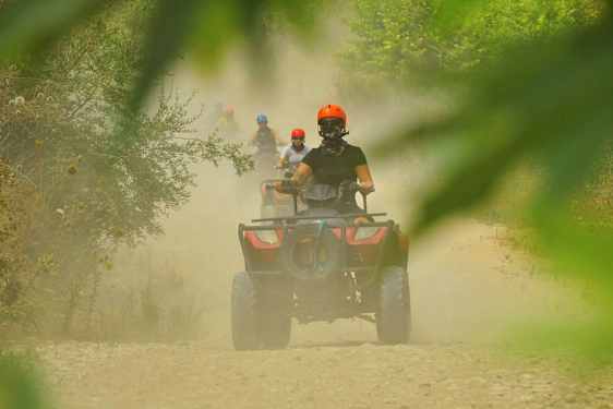 Personer som kör fyrhjulingar på en dammig grusväg omgiven av växtlighet. (AI-genererad text)