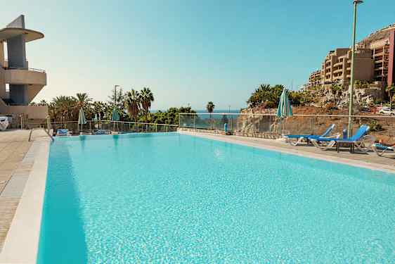 En stor pool omgiven av solstolar och parasoller, med utsikt mot havet och frodig växtlighet. (AI-genererad text)