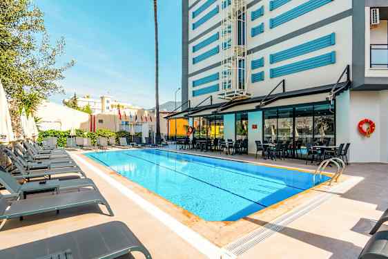 En utomhuspool med solstolar och ett hotell i bakgrunden. (AI-genererad text)