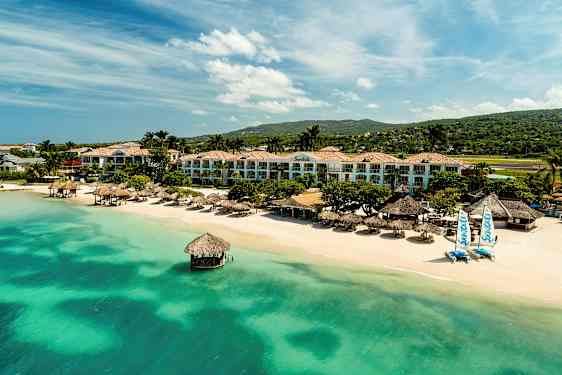 Resort vid strand med grönblått vatten, palmer och byggnader. (AI-genererad text)