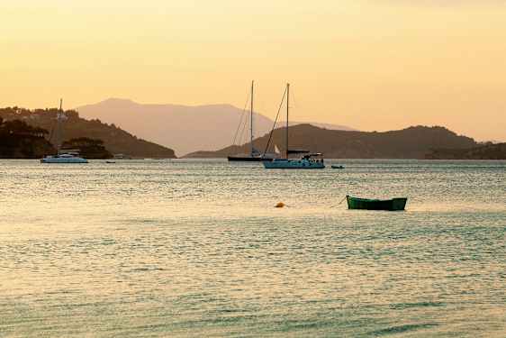 Bild av en stilla vik vid solnedgången med segelbåtar och en grön båt i förgrunden. (AI-genererad text)