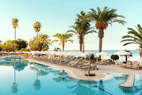 Poolområde med solstolar, parasoller och palmer nära havet. (AI-genererad text)