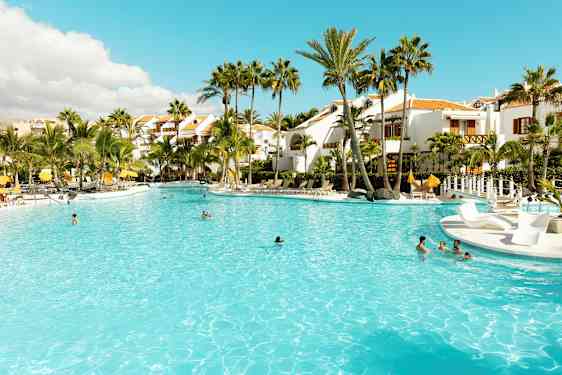 Stor pool omgiven av palmer och vita byggnader. (AI-genererad text)