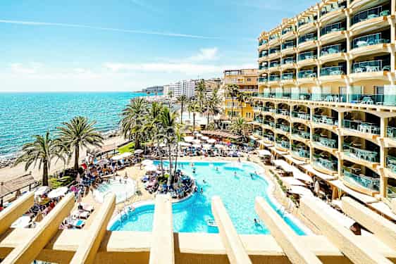 En solig hotellträdgård med pooler, palmer och utsikt över havet. (AI-genererad text)