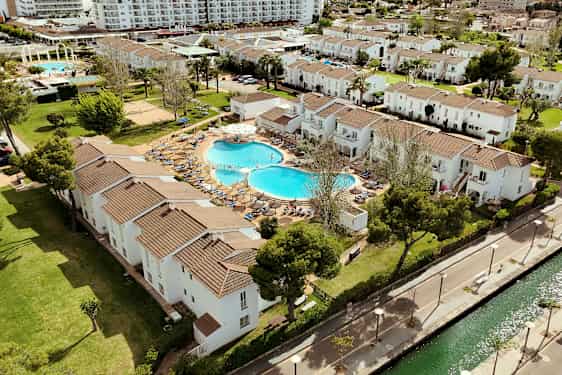 En flygbild av ett semesterkomplex med vita byggnader, en pool och grönområden. (AI-genererad text)