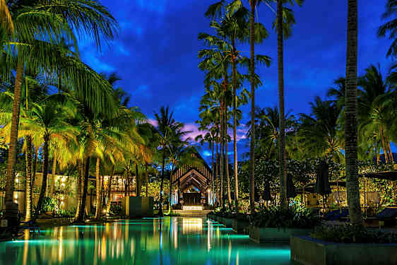 En kvällsbild på en upplyst pool och höga palmer vid en resort. (AI-genererad text)