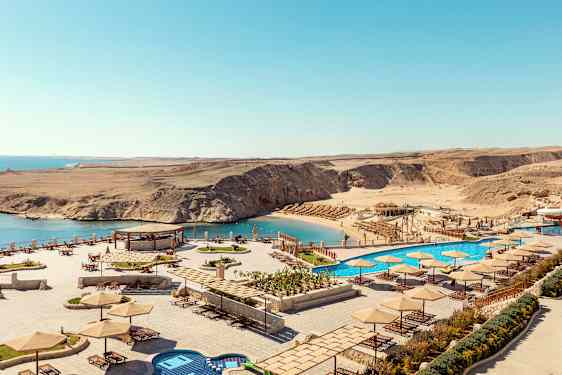 Vy över en strand med parasoller och solstolar, samt en pool bredvid havet. (AI-genererad text)