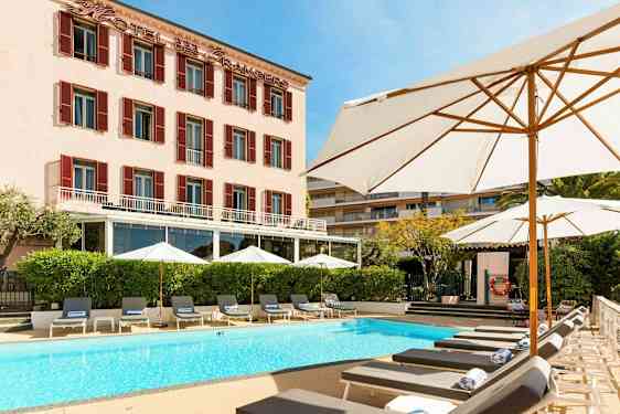 Hotellbyggnad med pool och solstolar framför. (AI-genererad text)