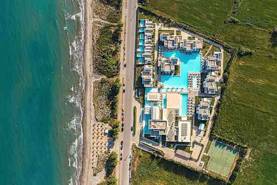 Flygbild över en semesterort med pooler och byggnader nära havet. (AI-genererad text)