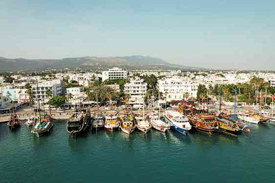 Hamnen med flera båtar förtöjda och en stad med vita byggnader i bakgrunden. (AI-genererad text)