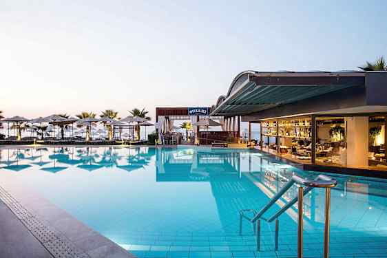 En stor pool vid en hotellrestaurang med utsikt över havet. Solstolar och parasoller omger området. (AI-genererad text)