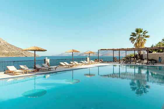 En utomhuspool med solstolar och parasoller vid sidan, samt havsutsikt i bakgrunden. (AI-genererad text)