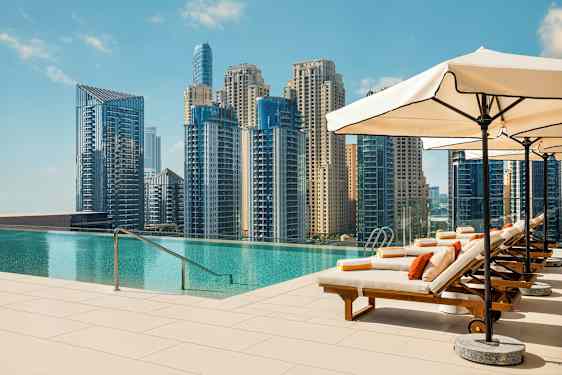 Solstolar vid en infinitypool med utsikt över en stad med höga byggnader. (AI-genererad text)