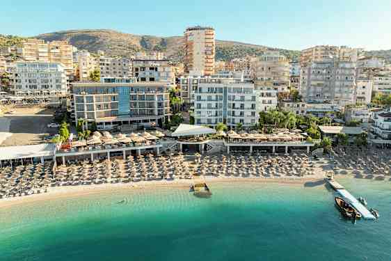 Vy över strand med solstolar och hotellbyggnader i bakgrunden. (AI-genererad text)