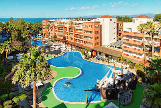 Hotellområde med stor pool, omgiven av palmer och byggnader. (AI-genererad text)