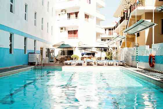 Utomhuspool med solstolar och parasoller, omgiven av byggnader. (AI-genererad text)