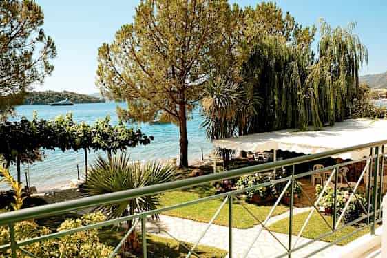 Utsikt över en trädgård med grönskande växter, träd och havet i bakgrunden. (AI-genererad text)