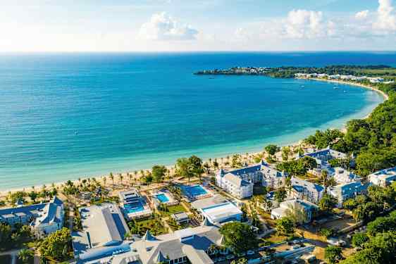 Bild av en kuststräcka med turkost vatten, en vit sandstrand och hotellbyggnader i närheten. (AI-genererad text)